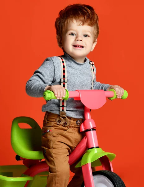 Ruiva menino na bicicleta sobre um fundo de cor laranja isolado — Fotografia de Stock