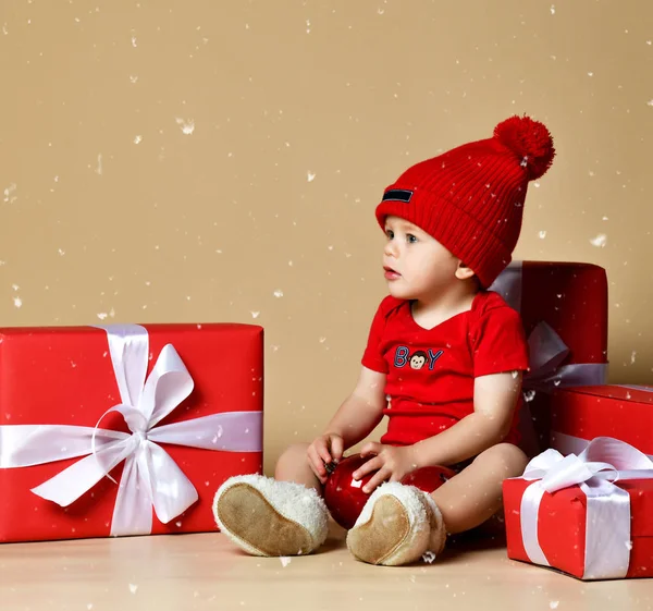 Criança de chapéu vermelho com pilhas de caixas de presente em torno sentado no chão . — Fotografia de Stock