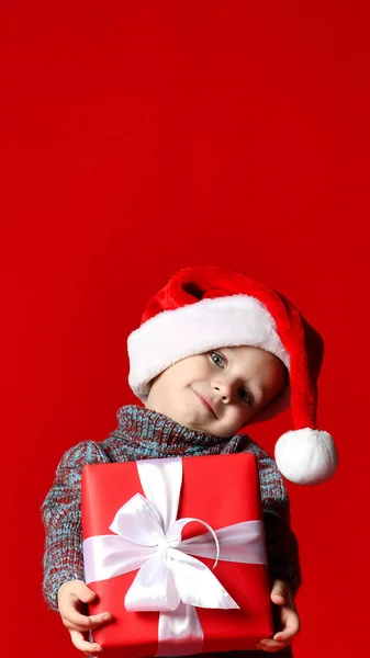 Legrační usmívající se dítě v Santa red hat v ruce drží vánoční dárek. — Stock fotografie