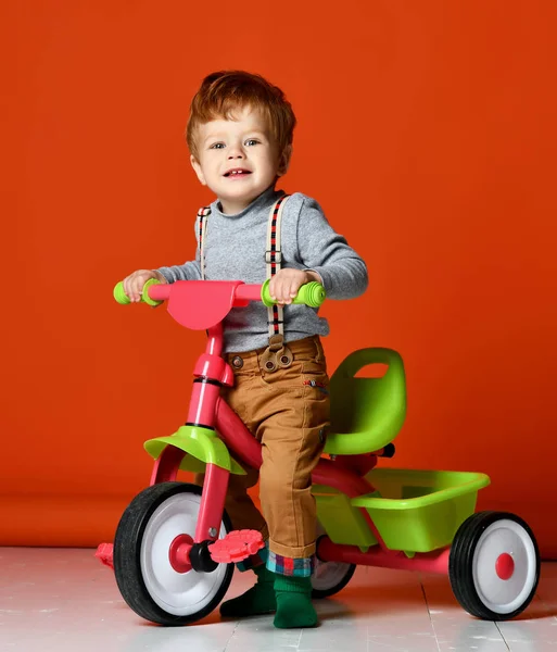 Ruiva menino na bicicleta sobre um fundo de cor laranja isolado — Fotografia de Stock