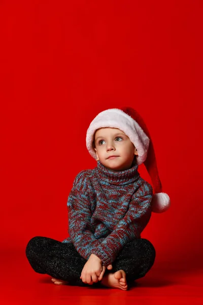 Menino em Papai Noel chapéu retrato sonhos de presentes em um fundo vermelho — Fotografia de Stock