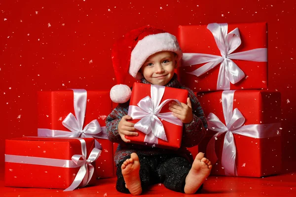 Sorrindo criança engraçada em Santa chapéu vermelho segurando presente de Natal na mão. Conceito de Natal. — Fotografia de Stock