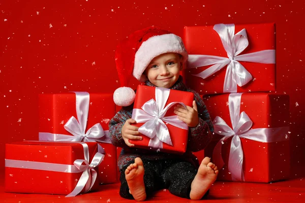 Smiling funny child in Santa red hat holding Christmas gift in hand. Christmas concept. — Stock Photo, Image