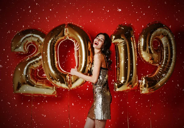 Retrato de bela menina sorridente em brilhante vestido dourado jogando Confetti, se divertindo com balões de ouro 2019 — Fotografia de Stock