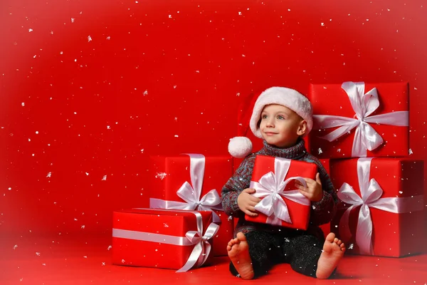 Усміхнена смішна дитина в червоному капелюсі, що тримає подарунок на Різдво в руці. Новорічна концепція . — стокове фото