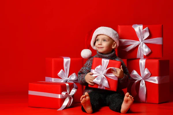 Glimlachend grappig kind in Santa rode hoed met kerstcadeau in de hand. Kerstconcept. — Stockfoto