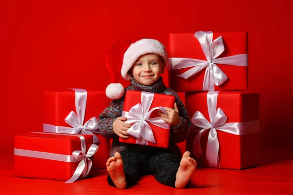 Smiling funny child in Santa red hat holding Christmas gift in hand. Christmas concept. — Stock Photo, Image