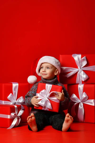 Sorrindo criança engraçada em Santa chapéu vermelho segurando presente de Natal na mão. Conceito de Natal. — Fotografia de Stock