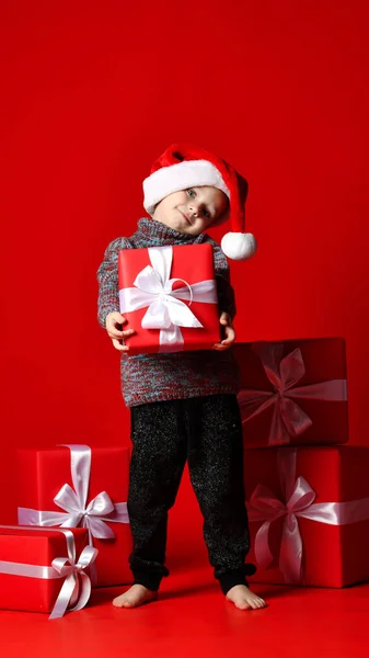 Criança sorrindo engraçado em Santa chapéu vermelho segurando presente de Natal na mão . — Fotografia de Stock