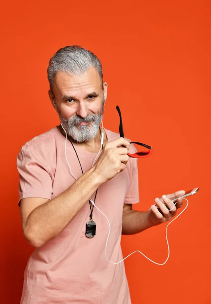 Homem sênior ouvindo música em fones de ouvido isolados em fundo laranja — Fotografia de Stock