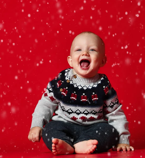 Маленький усміхнений хлопчик, одягнений у теплий светр, сидить на червоному тлі — стокове фото