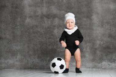 küçük çocuk bir yana, bacaklarını siyah ve beyaz bir futbol yakınındaki şaşırmış görünüyor. Beyaz pamuk şapka ve siyah bir elbise giyen