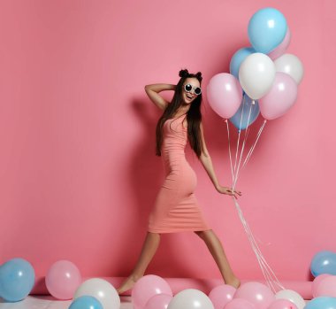 Yaygın olarak gülümseyen ve mavi ve pembe baloons ile oynarken bir stüdyoda şirin sarışın kız ayakta Close-up.