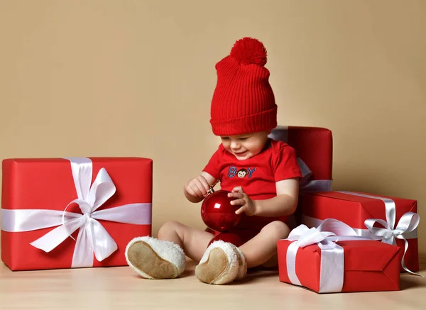 Дитина в червоному капелюсі зі стопами теперішніх коробок навколо сидить на підлозі . — стокове фото
