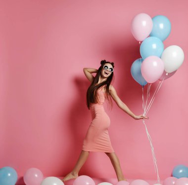 Yaygın olarak gülümseyen ve mavi ve pembe baloons ile oynarken bir stüdyoda şirin sarışın kız ayakta Close-up.