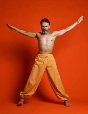 Yaşlı sakallı adamın yoga pozları verip bacaklarını açtığı bir stüdyo fotoğrafı.