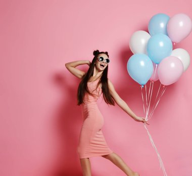 Yaygın olarak gülümseyen ve mavi ve pembe baloons ile oynarken bir stüdyoda şirin sarışın kız ayakta Close-up.