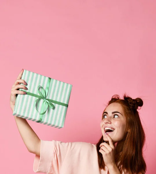 Portret van een vrij lachende roodharige meisje geschenkdoos houden en kijken, geïsoleerd op kleur roze achtergrond — Stockfoto