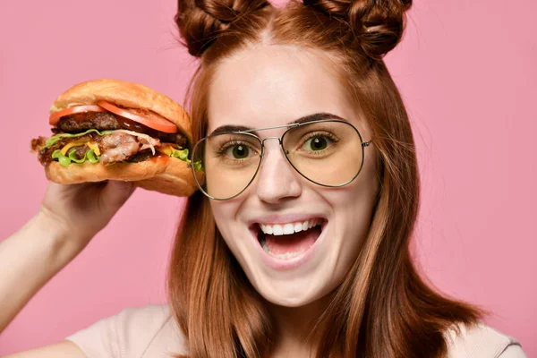 Pembe arka plan üzerinde izole burger yemek aç bir genç kadın portresi kapatın — Stok fotoğraf