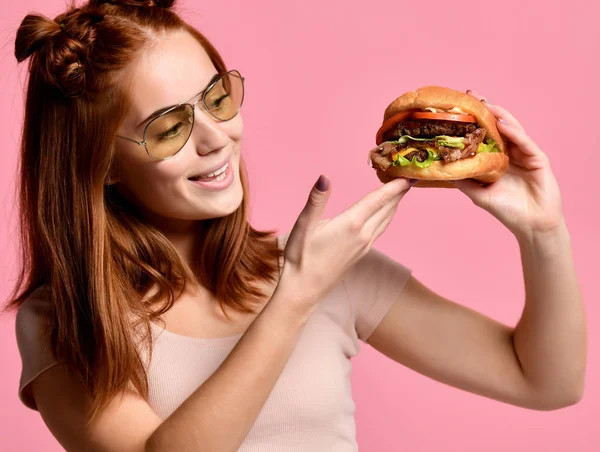Pembe arka plan üzerinde izole burger yemek aç bir genç kadın portresi kapatın — Stok fotoğraf