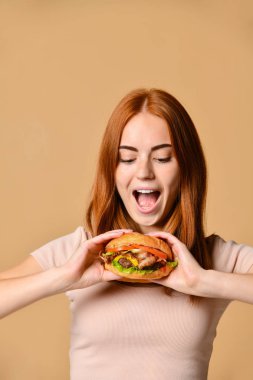 Portre aç genç bir kadının çıplak arka plan üzerinde izole hamburger yeme kapatmak