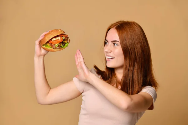 Close up portrait of a hungry young woman eating burger isolated over nude background