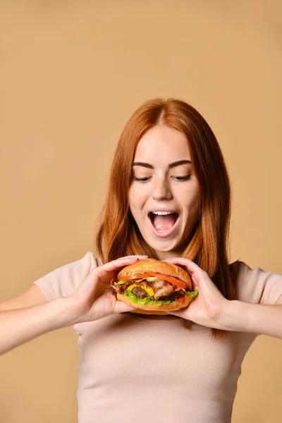 Primer plano retrato de una joven hambrienta comiendo hamburguesa aislada sobre fondo desnudo —  Fotos de Stock