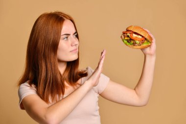 Portre aç genç bir kadının çıplak arka plan üzerinde izole hamburger yeme kapatmak