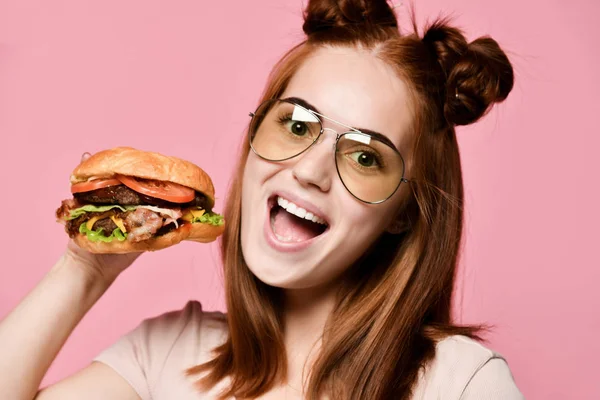 Horizontal studio shot of pretty young woman holding a burger and a glass of soda. — Stock Photo, Image