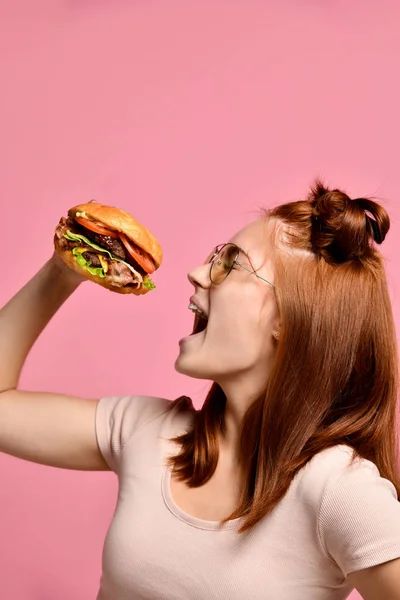 Plan studio horizontal d'une jolie jeune femme tenant un hamburger et un verre de soda . — Photo