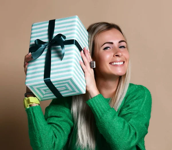 Portret van een vrij lachende blond meisje geschenkdoos houden en kijken, geïsoleerd op kleur beige achtergrond — Stockfoto