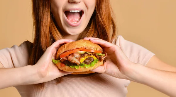 Close up portrait of a hungry young woman eating burger isolated over nude background — Stock Photo, Image