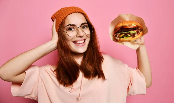 Närbild porträtt av en hungrig ung kvinna äta burger isolerade över rosa bakgrund — Stockfoto