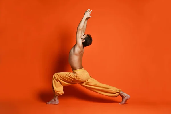Vecchio che pratica yoga facendo esercizi di stretching contro sfondo arancione — Foto Stock