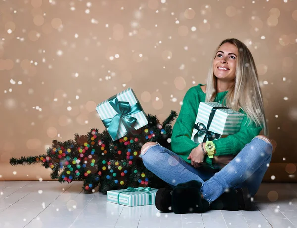 young woman sitting on the floor near fir Christmas tree and dreaming about present, future, gifts and waiting a miracle at this xmas night