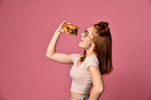 Horisontella studio skott av vackra unga kvinna som håller en hamburgare och ett glas läsk. — Stockfoto
