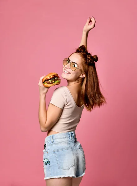 Horizontal studio shot of pretty young woman holding a burger