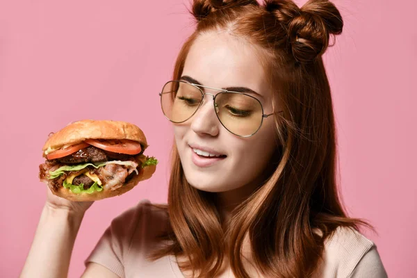 Close up portrait of a hungry young woman eating burger isolated over pink background — Stock Photo, Image