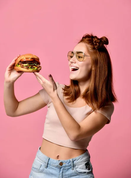 Potret dekat seorang wanita muda yang lapar makan burger terisolasi di atas latar belakang putih — Stok Foto