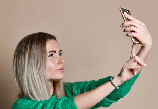 Retrato de cerca de la joven mujer rubia de moda alegre en ropa de jersey hace selfie en el teléfono inteligente, sobre fondo beige — Foto de Stock