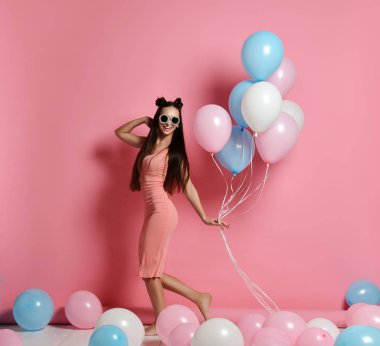 Yaygın olarak gülümseyen ve mavi ve pembe baloons ile oynarken bir stüdyoda şirin sarışın kız ayakta Close-up.