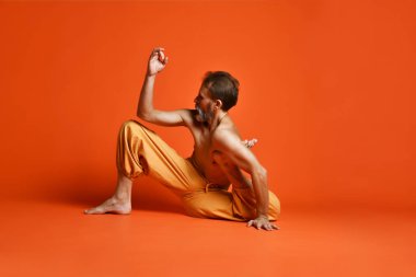 Turuncu arka planı germe yapıyor yaşlı adam pratik yoga egzersizleri