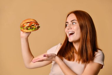 Portre aç genç bir kadının çıplak arka plan üzerinde izole hamburger yeme kapatmak