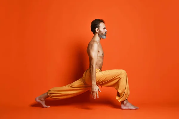 Viejo practicando yoga haciendo ejercicios de estiramiento sobre fondo naranja — Foto de Stock