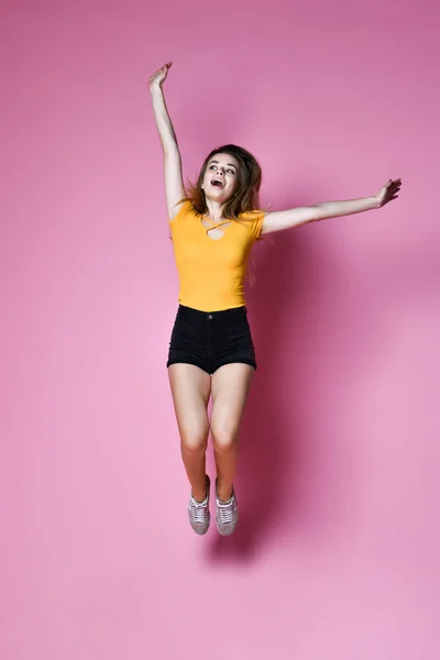 照片中快乐而积极的女孩跳到空中，看着被粉色背景隔离的相机. — 图库照片
