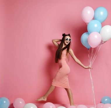 Yaygın olarak gülümseyen ve mavi ve pembe baloons ile oynarken bir stüdyoda şirin sarışın kız ayakta Close-up.