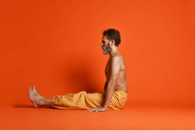 Turuncu arka planı germe yapıyor yaşlı adam pratik yoga egzersizleri