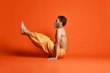 Turuncu arka planı germe yapıyor yaşlı adam pratik yoga egzersizleri