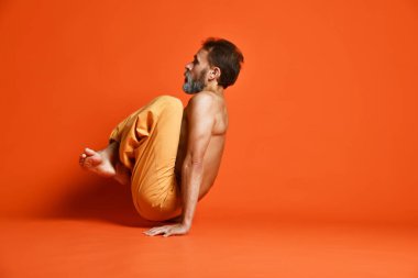 Turuncu arka planı germe yapıyor yaşlı adam pratik yoga egzersizleri