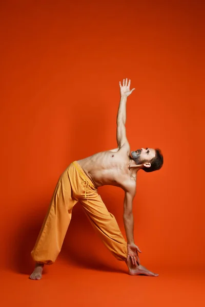 Fitness senior hombre haciendo ejercicio yoga asana pierna aislada sobre un fondo naranja — Foto de Stock